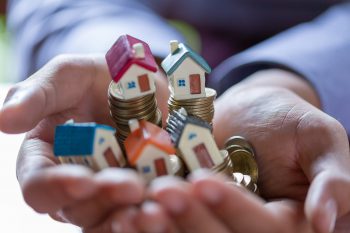 House model and coin money on hand for finance and banking concept.